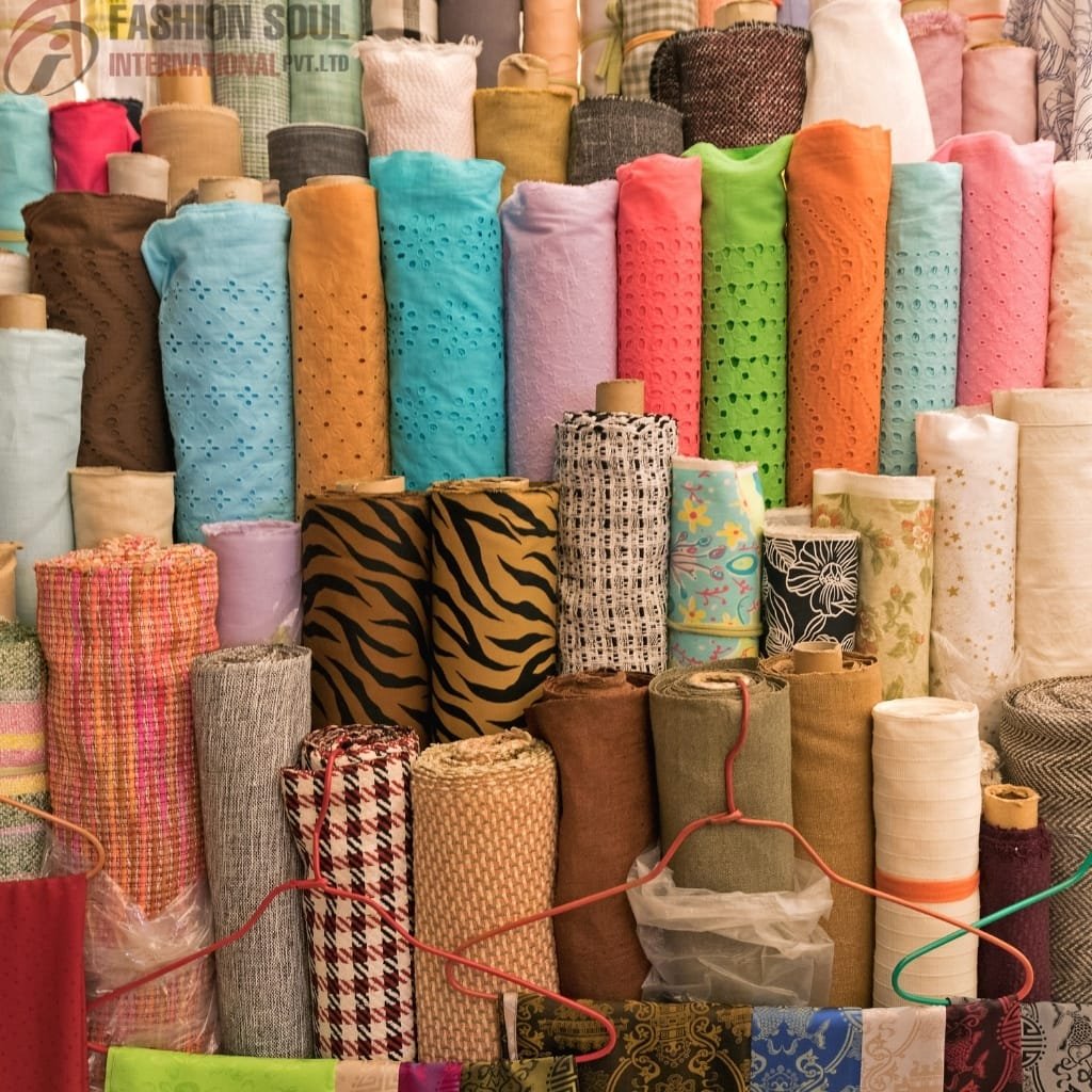 An assortment of colorful fabric rolls, including patterned, solid, and textured materials arranged in a display, with some stacked vertically and others rolled and placed side by side.