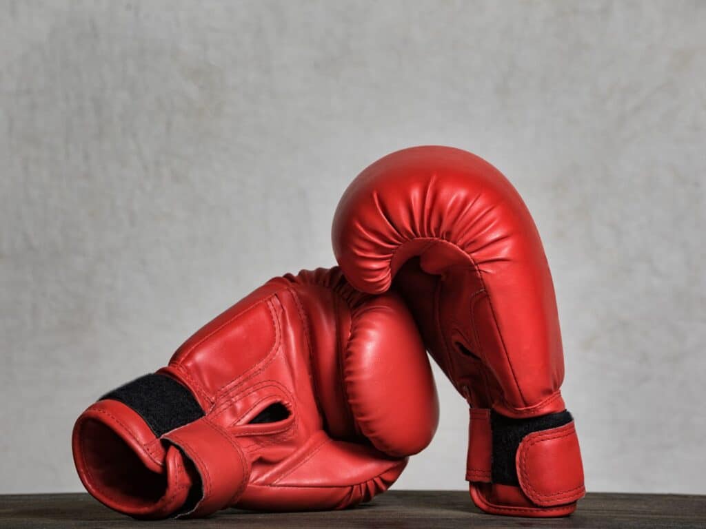 A pair of red boxing gloves placed on a wooden surface with a plain background.