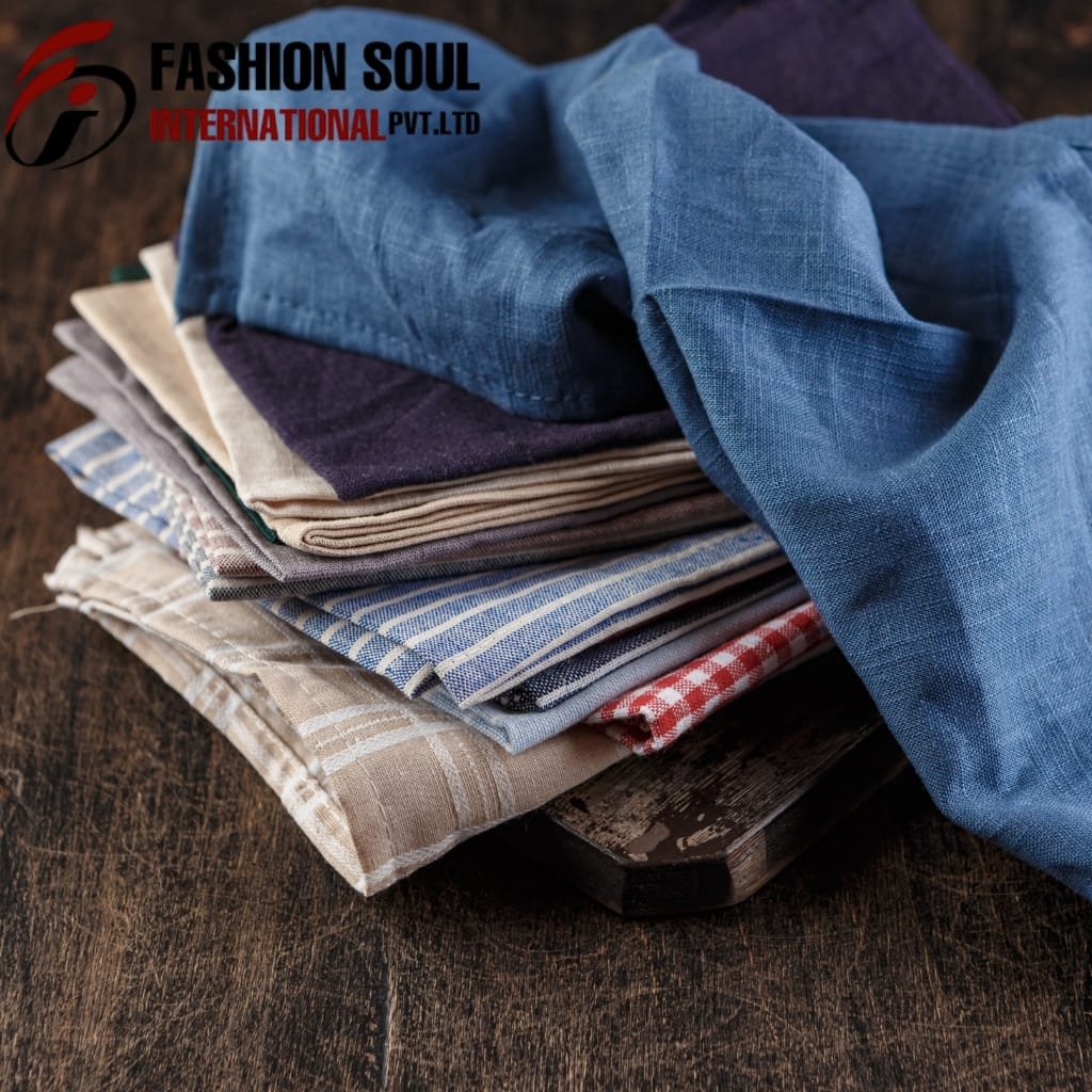 A neatly stacked pile of various fabric swatches, including plaid, striped, and solid colors, placed on a dark wooden surface.