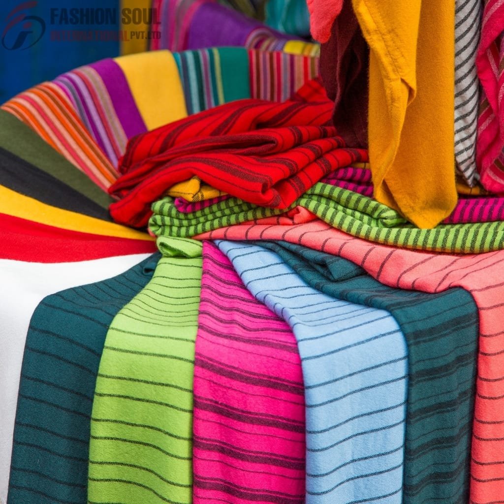 A colorful display of folded fabric and clothing with various bright stripes and patterns, including yellow, red, pink, green, blue, and black.