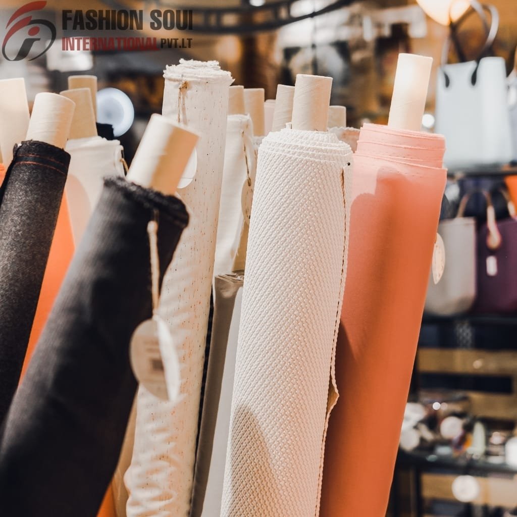  Rolled fabrics in black, white, and peach colors displayed on a rack in a boutique store, with blurred background items.