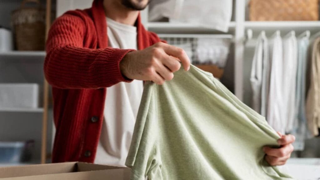 A person in a red cardigan holds up a light green fabric, inspecting it in a closet or laundry space.