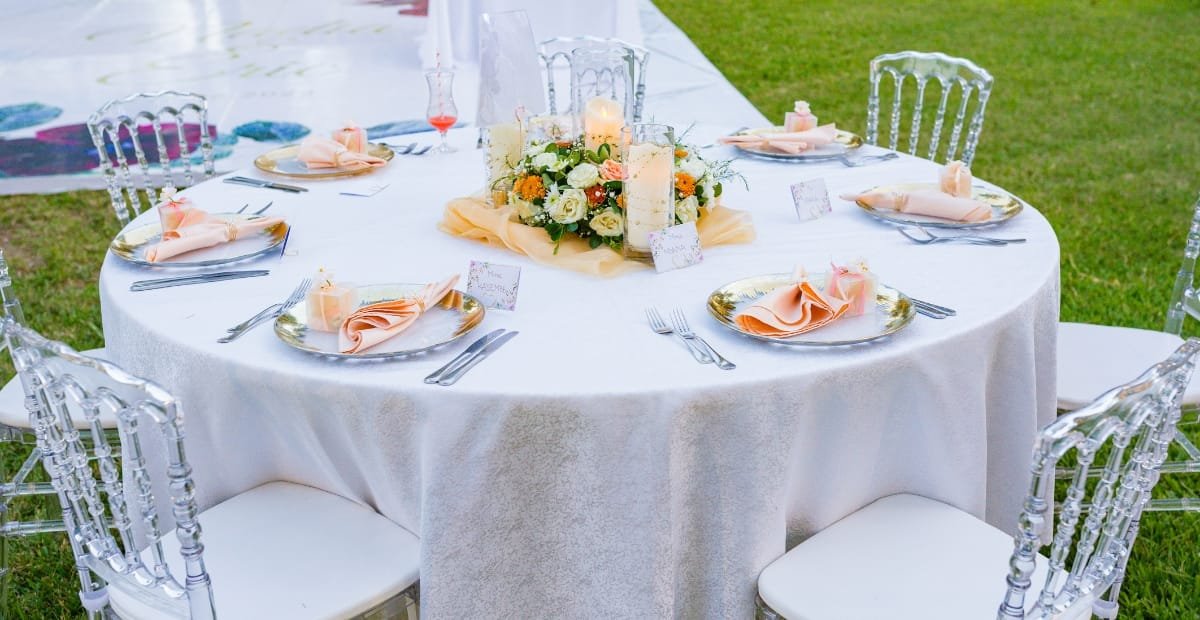 Elegant round table with inexpensive white table linens, floral centerpiece, candles, and neatly arranged place settings.