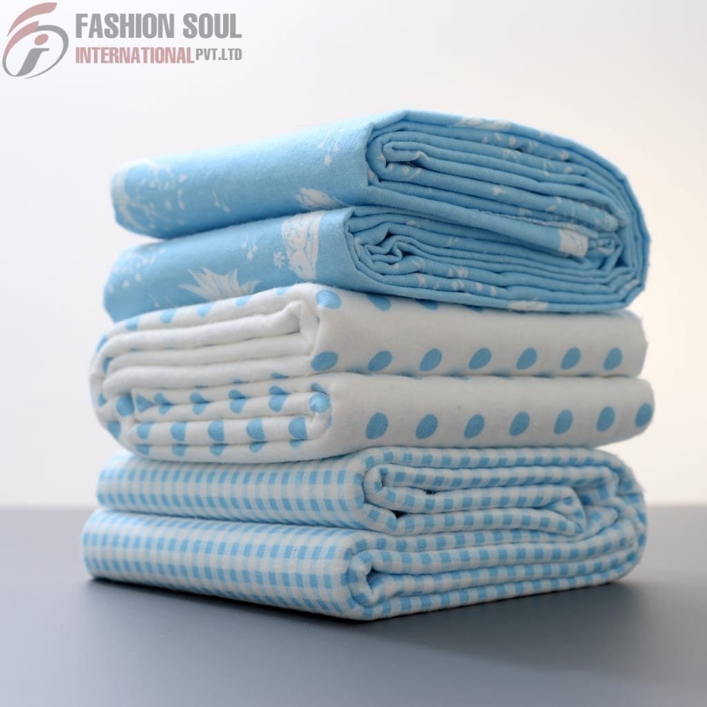 A neatly folded stack of three blue and white patterned fabrics, with the top one rolled.
