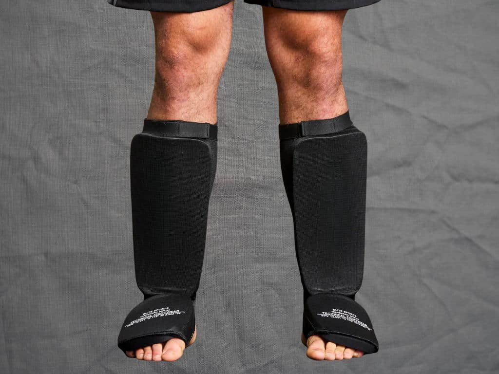 Pair of black MMA shin guards worn by a person, showing their padded design and straps for secure fit.