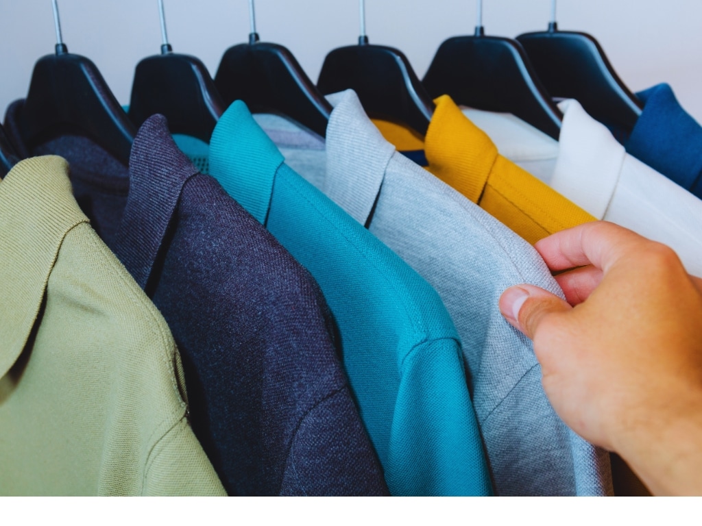 A person browsing colorful polo shirts hanging on a rack, showcasing various styles and colors.