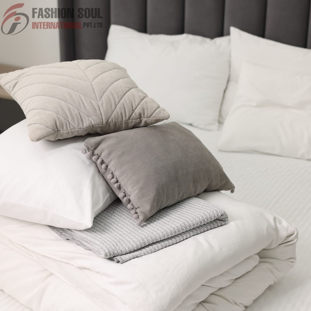 A neatly made bed with white pillows, a folded blanket, and two decorative pillows in shades of beige and gray, set against a dark upholstered headboard.