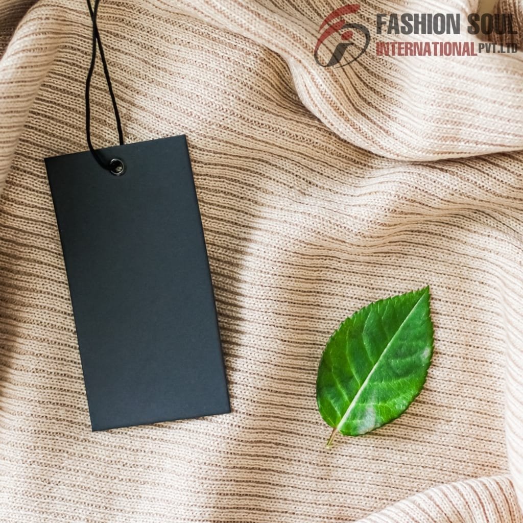 A textured beige fabric with a black price tag hanging from a black string next to a bright green leaf.