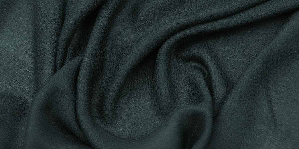 Close-up of dark green fabric with soft folds and a smooth texture.