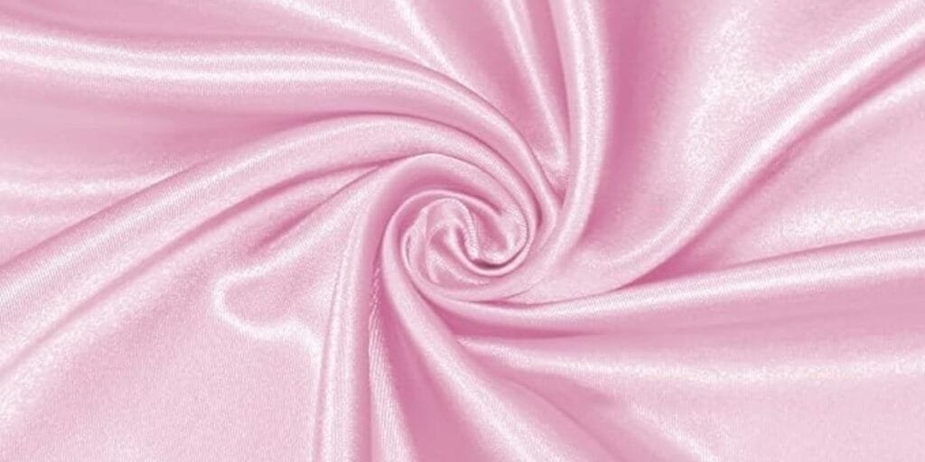 Close-up of shiny light pink satin fabric twisted into a swirl pattern.