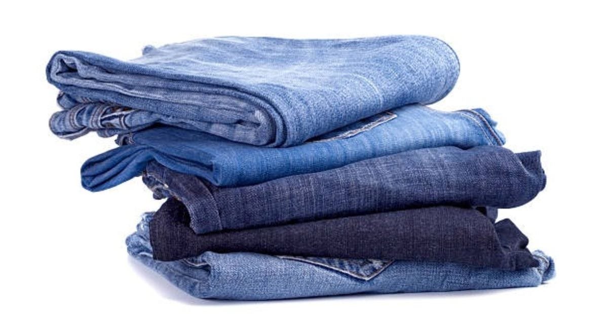 A stack of five folded denim jeans in various shades of blue.