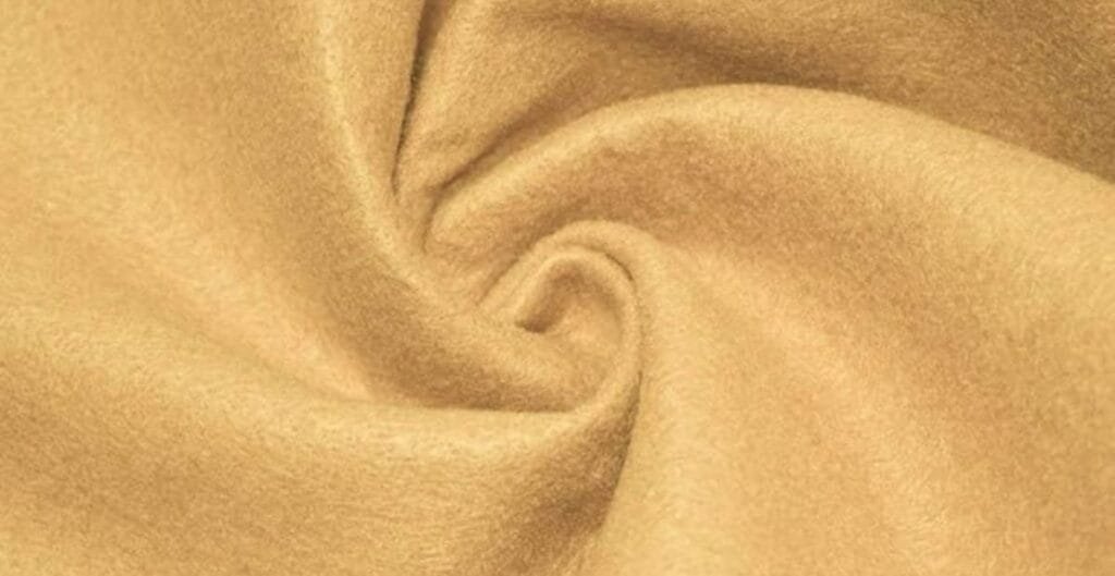 Close-up of light brown wool fabric with a soft, fuzzy texture and a twisted fold pattern.
