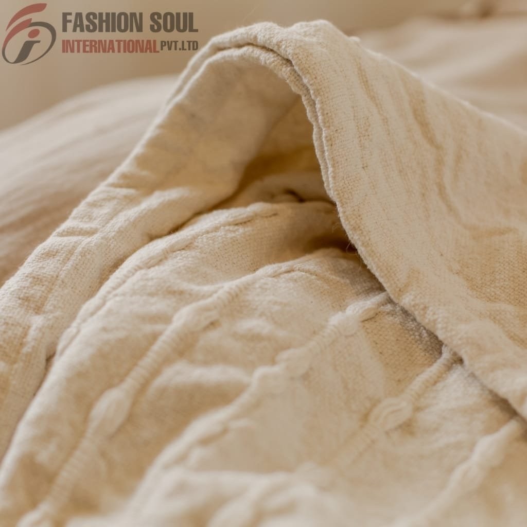 Close-up of beige, textured fabric with visible stitching and folds, showing a soft, woven material.