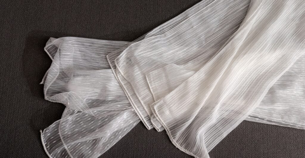 White sheer fabric with thin vertical stripes laid out on a dark surface.