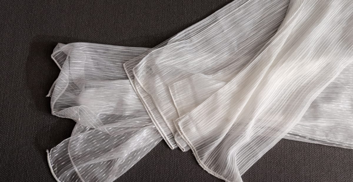 White sheer fabric with thin vertical stripes laid out on a dark surface.