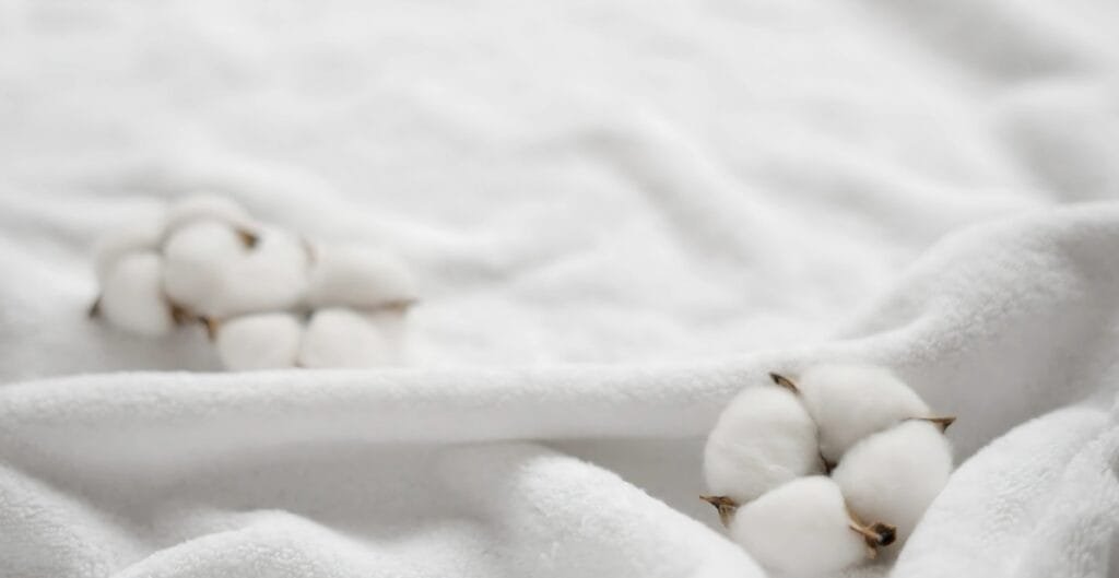 Close-up of white cotton bolls on a soft, white fabric background.