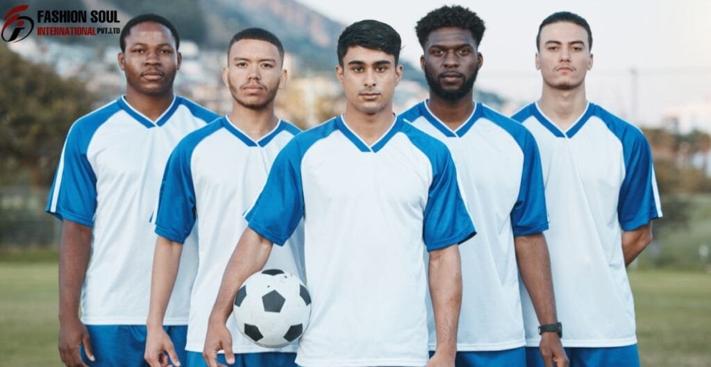 A group of five young male soccer players standing outdoors on a field, dressed in matching blue and white soccer uniforms. The player in the center is holding a soccer ball. There is a blurred background of trees and a field.