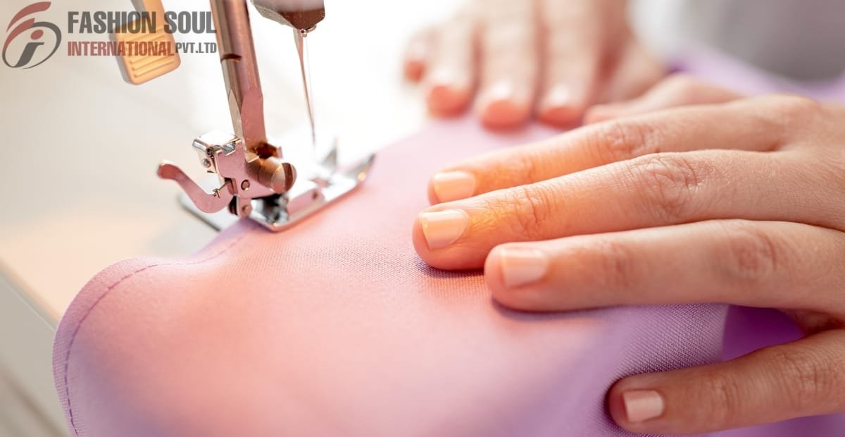 Close-up of a sewing machine stitching pink fabric, with a person's hand guiding the material.