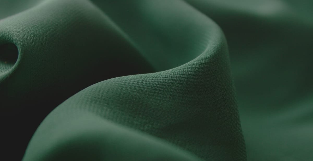 Close-up of smooth, dark green fabric with gentle folds and a subtle texture.