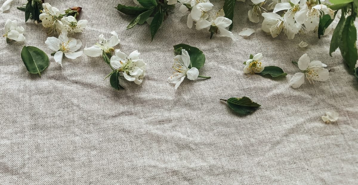 White flowers and green leaves scattered on a textured, light-colored fabric surface.