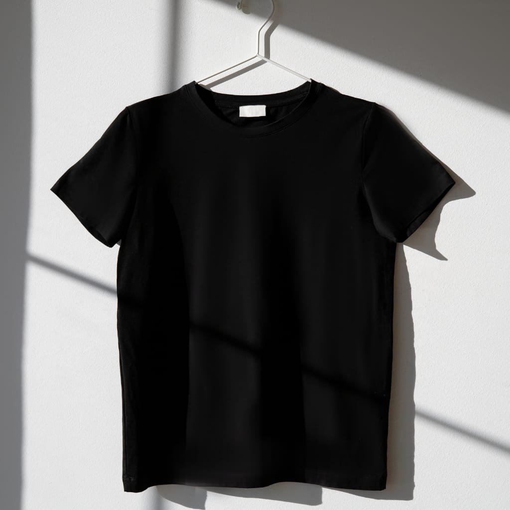 Plain black t-shirt hanging on a white hanger against a sunlit wall.
