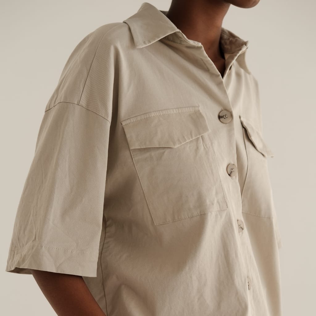 Close-up of a person wearing a beige button-up shirt with short sleeves and front flap pockets.