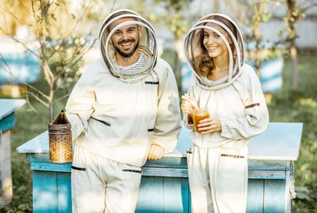 Front view of a heavy-duty bee suit with mesh veil, thick gloves, and boot covers laid out on a workshop table.