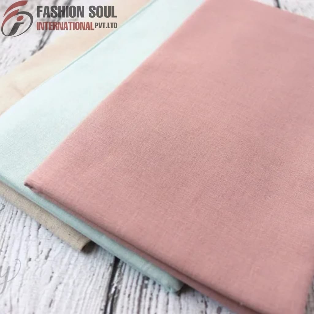  Two folded pieces of fabric, one light pink and one light blue, placed on a white wooden surface. The fabrics are smooth and plain with no visible patterns