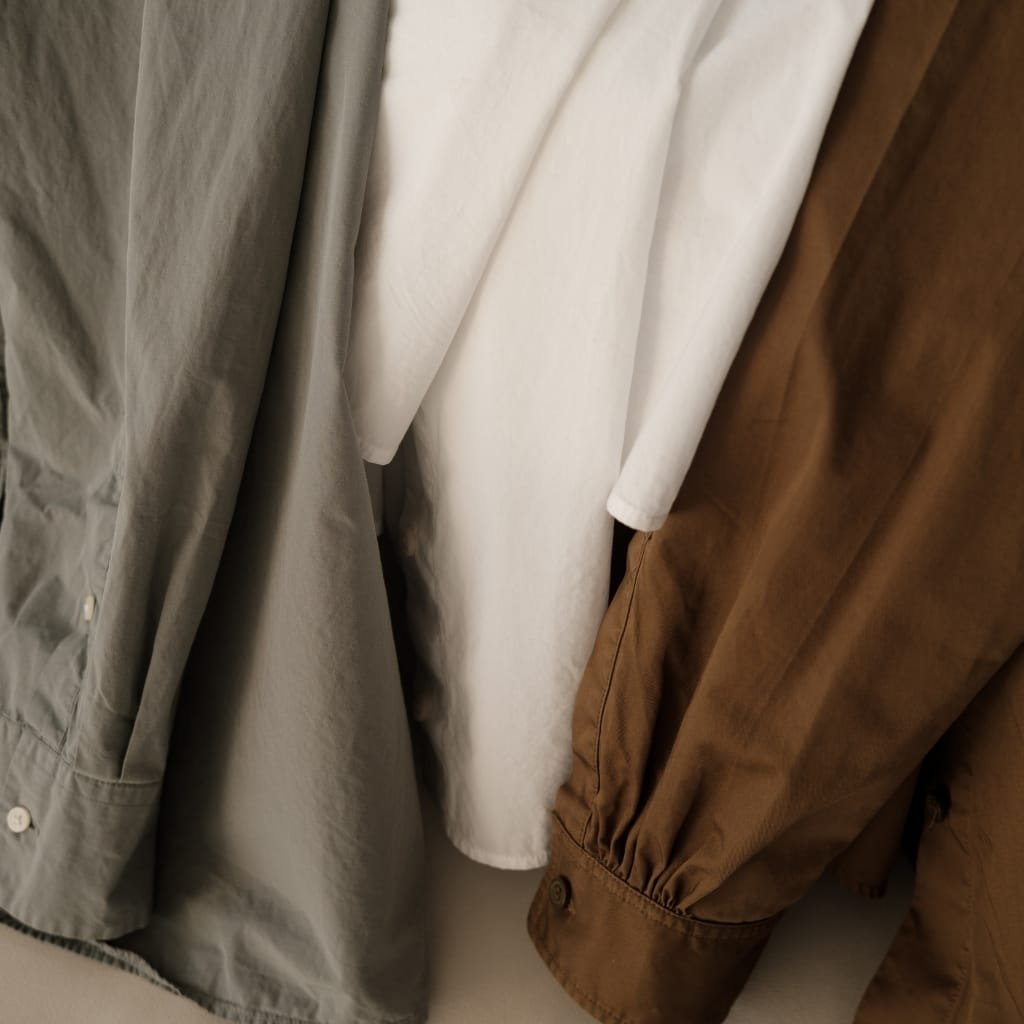 Close-up of three shirts in gray, white, and brown tones hanging side by side.