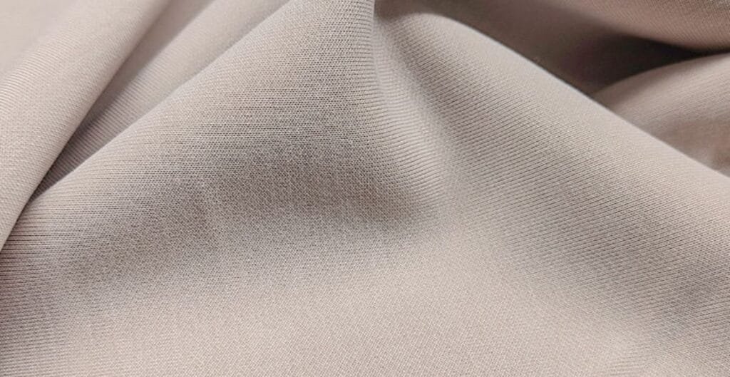 Close-up of smooth beige fabric with fine texture and soft folds.