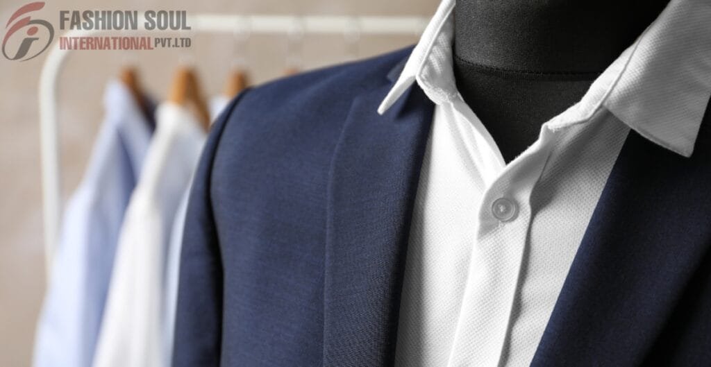 A close-up view of a dark blue suit jacket worn over a white dress shirt on a mannequin, with blurred shirts hanging on a rack in the background. A logo reading “FASHION SOUL INTERNATIONAL PVT. LTD” appears in the top-left corner.