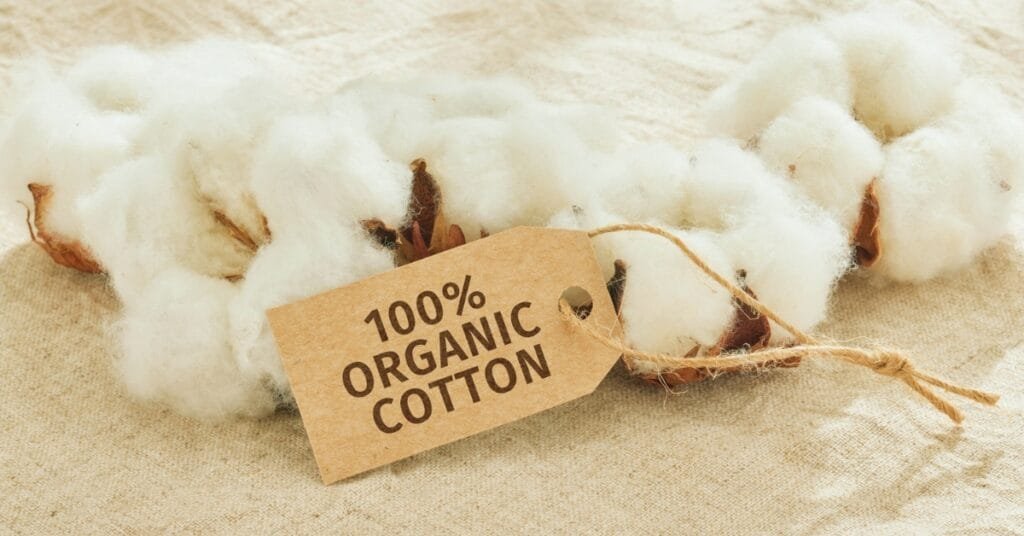 “A close-up of fluffy cotton with a brown tag that reads ‘100% ORGANIC COTTON’ tied with twine.”