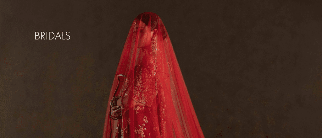 A person wearing a bright red veil or garment against a dark background, with the word “NOKA” or label in white on the left.