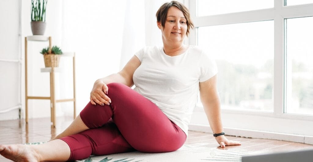 Woman in 3x yoga pants comfortably stretching on a mat