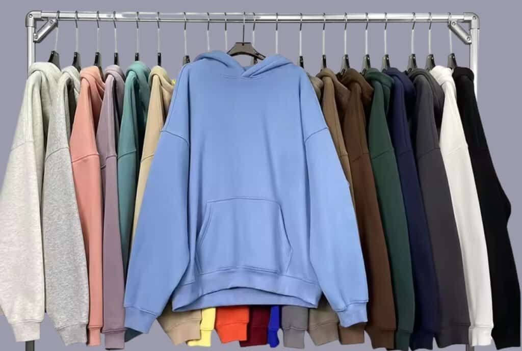 A cozy, oversized hoodie laid flat with visible customization options: embroidery on the chest, color-block sleeves, and a drawstring with metal aglets; soft fabric texture and roomy fit emphasized.