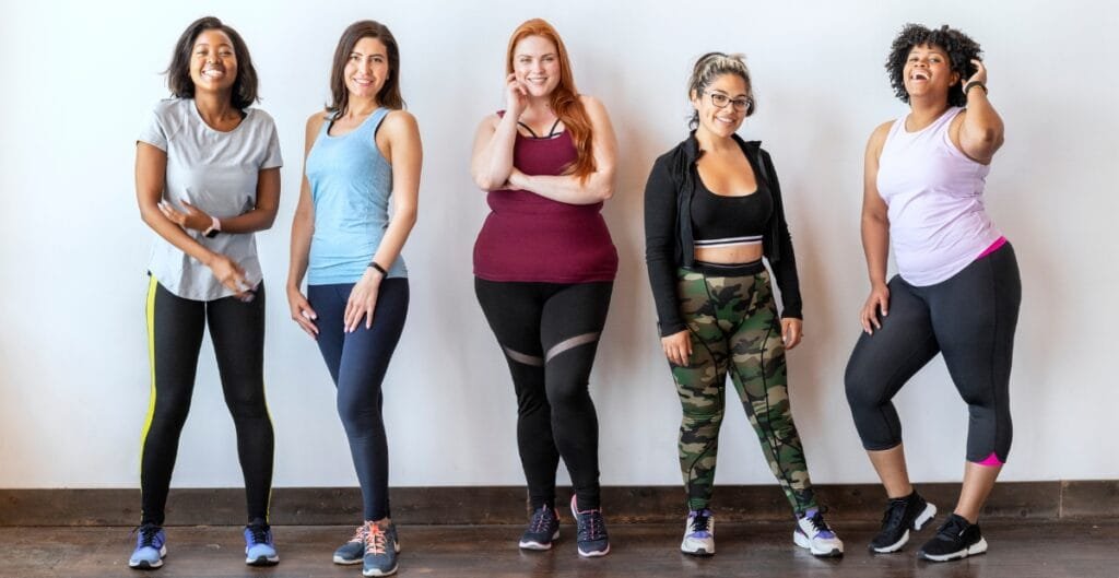 A confident plus-size woman wearing sleek black leggings, standing with hands on hips against a neutral backdrop.