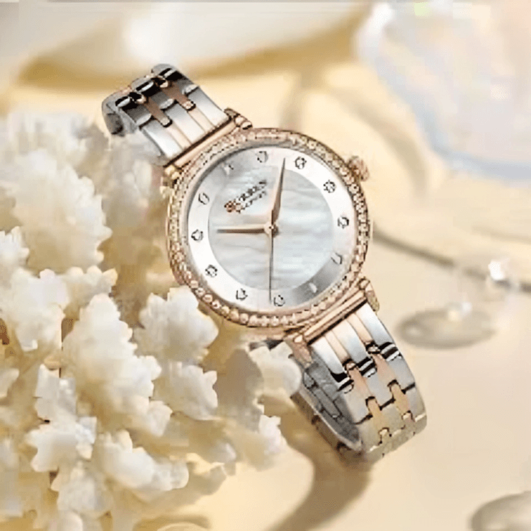 A stylish two-tone wristwatch with a rose gold and silver band, a bezel adorned with small crystals, and a mother-of-pearl dial, resting beside white coral.