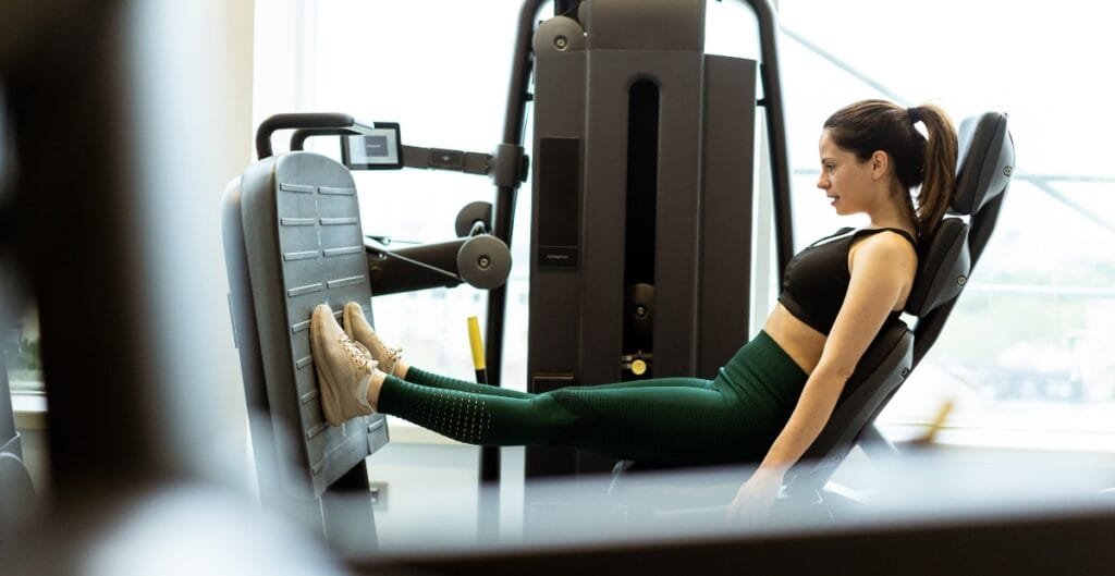 Woman wearing green gym leggings doing a leg press workout at the gym