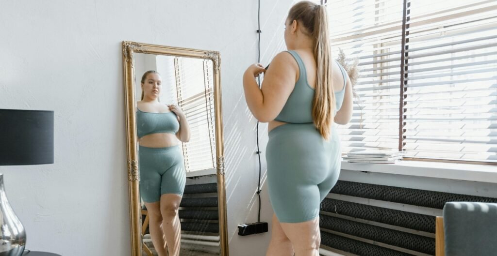 Plus-size woman wearing teal ladies plus shorts and matching top looking at her reflection in a mirror.