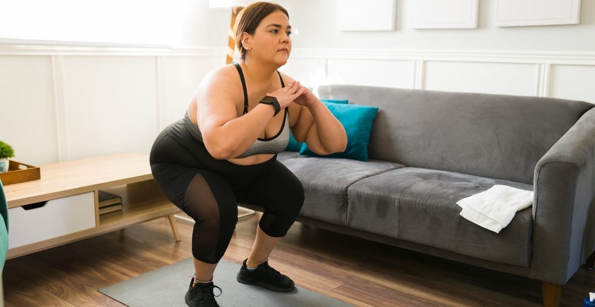 Woman in a plus-size workout onesie performing squats at home