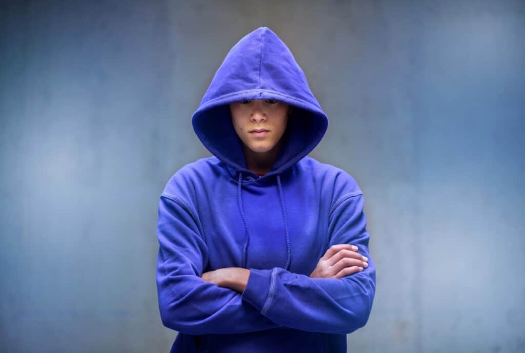A factory floor where workers sew and inspect high-quality hoodies, with branding concepts and fabric swatches laid out on a table in the foreground.