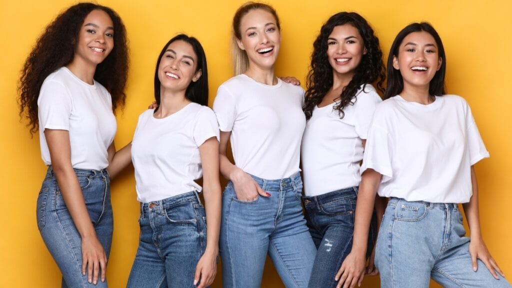A diverse group of curvy tweens posing together in white T-shirts and jeans with smiles on their faces.