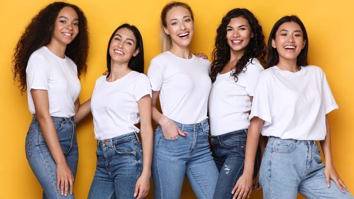 A diverse group of curvy tweens posing together in white T-shirts and jeans with smiles on their faces.
