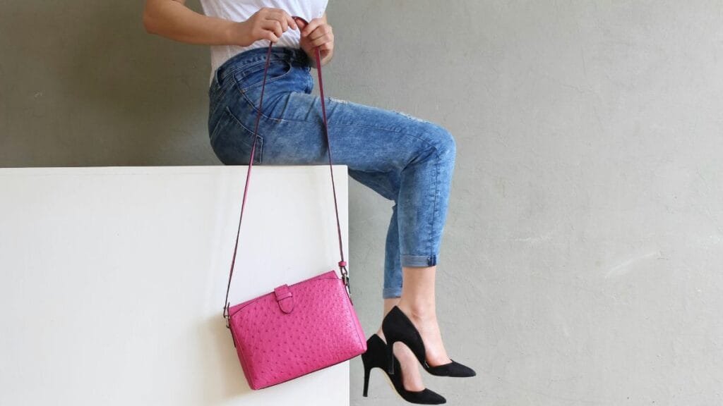 Woman wearing dressy slacks with a pink handbag and black heels, sitting on a white surface
