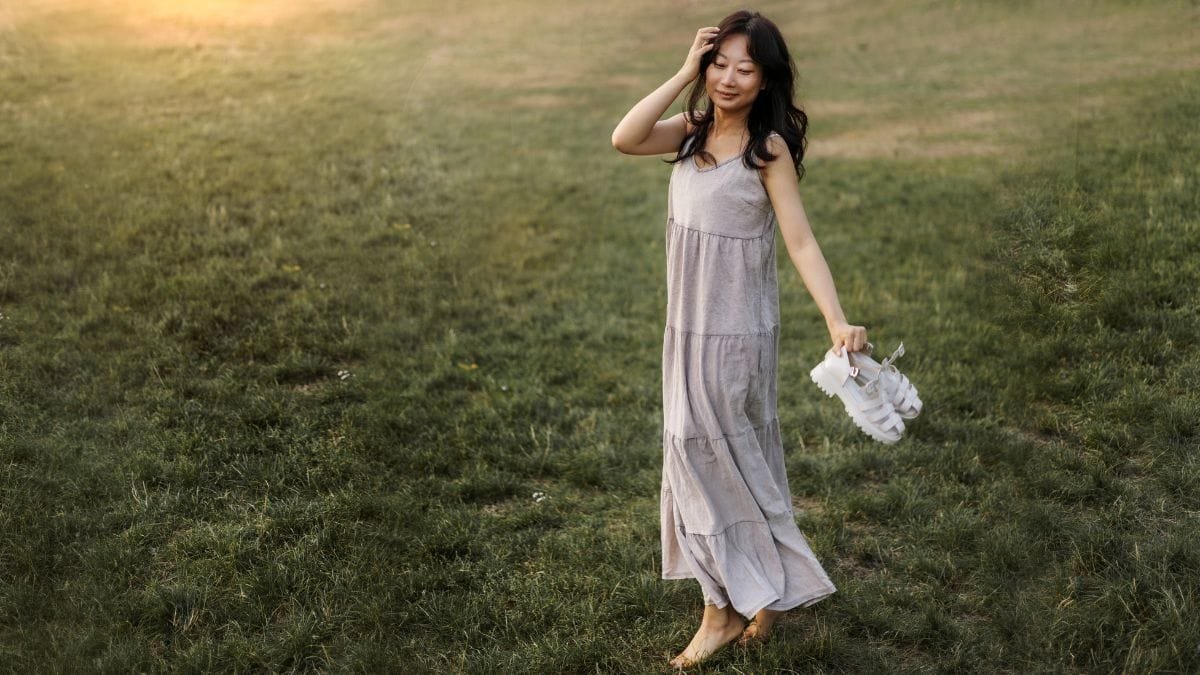 Woman wearing a light flowy midi dress standing on a grassy field at sunset