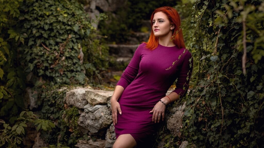 Red-haired woman in a mauve velvet dress leaning on rocks