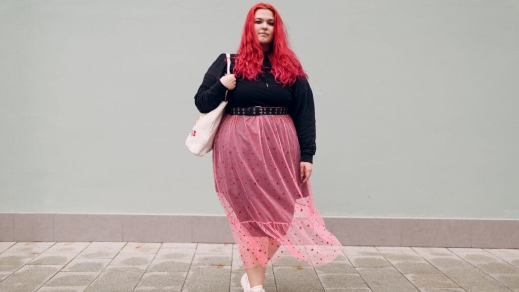 Plus-size woman wearing a starry pink skirt and black top, holding a bag.