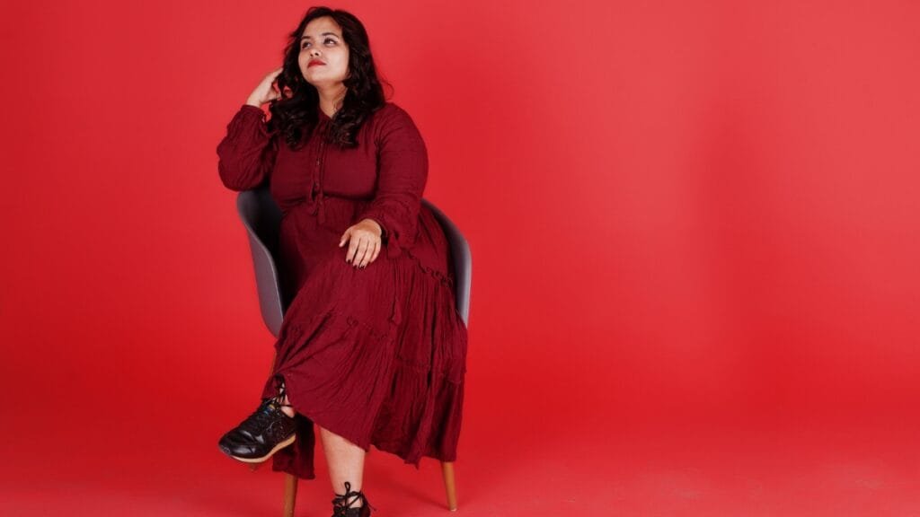Woman wearing a red plus size velvet dress posing confidently in a studio setting