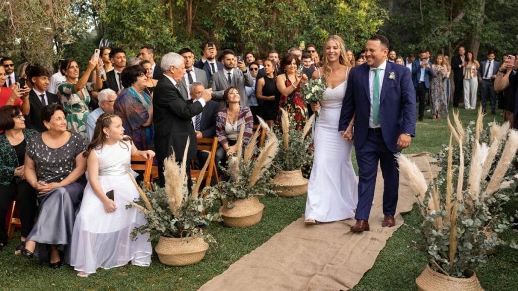Bride walking down the aisle in a white dress, with guests watching in an outdoor wedding ceremony