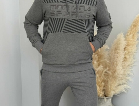 A person wearing a gray hoodie with a large front pocket and matching jogger pants, standing with hands in pockets.